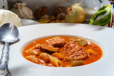 Bir bardak kırmızı şarapla servis edilen mozzarella peynirli soğan ve biberli kremalı İtalyan sosis çorbası.