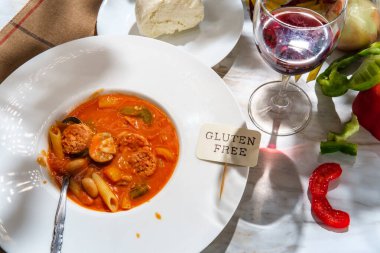 Bir bardak kırmızı şarapla servis edilen mozzarella peynirli soğan ve biberli kremalı İtalyan sosis çorbası.