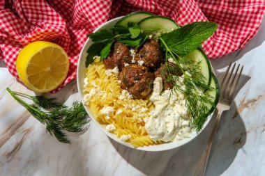 Yunan kuzu keftedes köftesi tzatziki yoğurt soslu Fusilli spiral makarna peyniri ve üzerine nane maydanozlu salatalık dilimleri ve dereotlu garnitür.