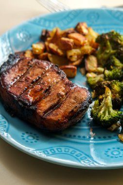 Kızarmış domuz pirzolası, yanında ızgara, yanında patates kızartması ve ızgara brokoli.