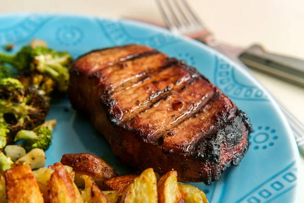 Kızarmış domuz pirzolası, yanında ızgara, yanında patates kızartması ve ızgara brokoli.