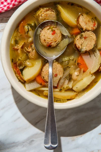 Vegetable chicken sausage noodle soup with chicken broth on marble kitchen table