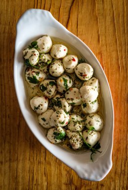 Salamura bocconcini bebek mozzarella salatası oval porselen lazanya pişirme kabında fesleğenle servis ediliyor.