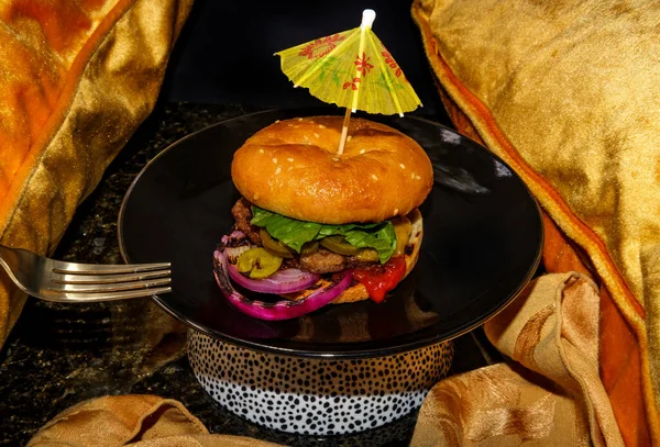 American food cheeseburger with pickled jalapeno peppers lettuce and grilled red onions cocktail umbrella toothpick