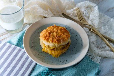 Sosisli yumurta ve peynirli bisküvili sandviç ve bir bardak süt.