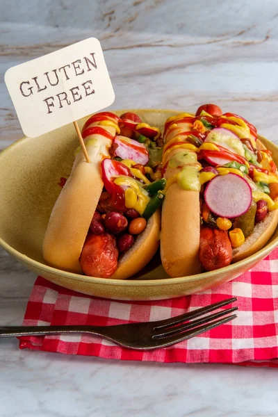 Fancy chili dogs topped with radishes mustard ketchup and green sauce on gluten-free buns