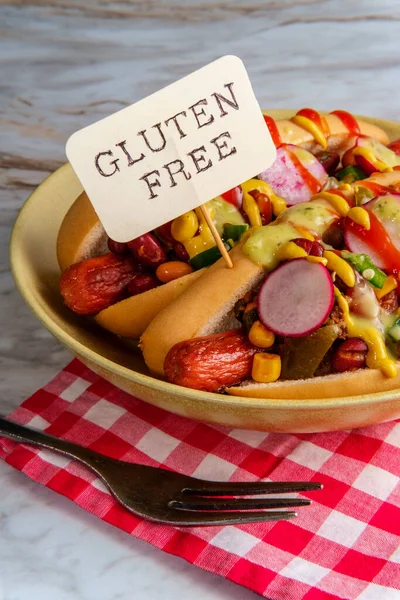 Fancy chili dogs topped with radishes mustard ketchup and green sauce on gluten-free buns