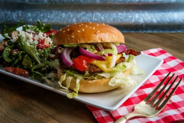 Yanında Yunan salatasıyla servis edilen gevrek domuz pastırmalı Angus bifteği çizburgeri.