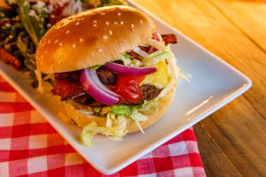 Yanında Yunan salatasıyla servis edilen gevrek domuz pastırmalı Angus bifteği çizburgeri.