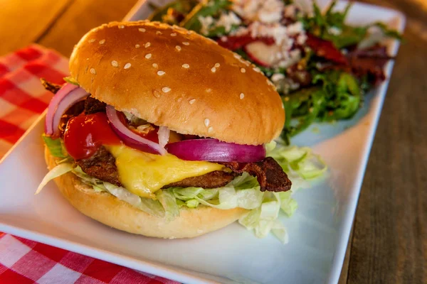 Angus beef cheeseburger topped with crispy bacon served with a side Greek salad