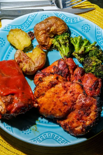 Plate of BBQ and grilled food including smashed potatoes Memphis rubbed chicken thighs charred broccoli and saucy ribs