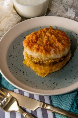 Sosisli yumurta ve peynirli bisküvili sandviç ve bir bardak süt.