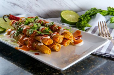 Mexican chicken and cheese rolled taco taquitos smothered in hot sauces and creme fraiche clipart