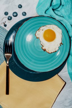 Sade, güneşli tarafı deniz mavisi tabağında kızarmış yumurta kahvaltısı.