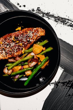 Çin portakallı tavuk smokin susam tohumlarıyla süslenmiş soyut siyah beyaz arka plan desenli sarımsaklı yeşil fasulye ile servis ediliyor.