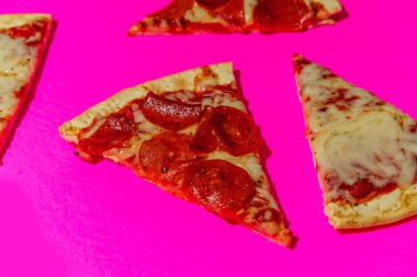 New York tarzı pizza dilimleri neon renkli arka planda sert ışıkla çekiliyor