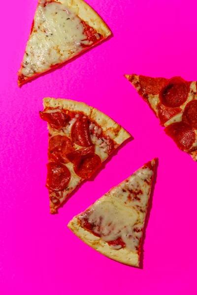 New York tarzı pizza dilimleri neon renkli arka planda sert ışıkla çekiliyor