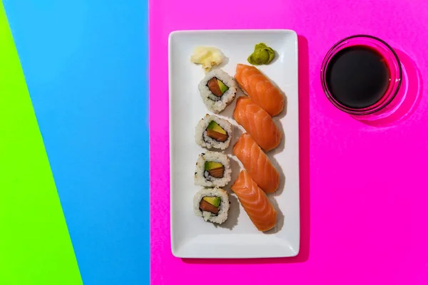 Combination Japanese Atlantic salmon sushi and nigiri with pickled ginger and wasabi on neon background