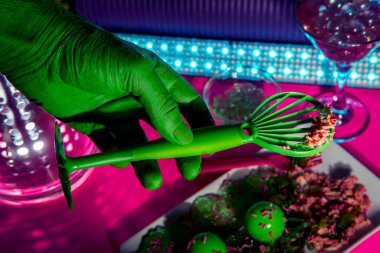 Uzaydan gelen bilim kurgu yeşil uzaylı süslü bir neon gece kulübünde yemek yiyor.