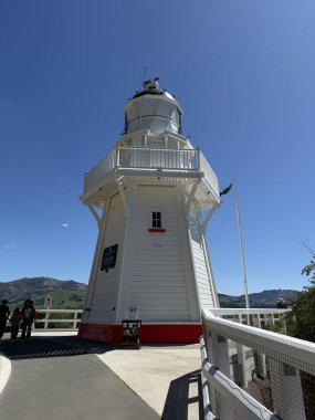 Limanın yanındaki Akaroa Deniz Feneri mavi gökyüzünün altında beyaz ahşap bir yapı gösteriyor. Deniz tarihini ve Akaroa Yeni Zelanda 'nın manzaralı sahil cazibesini simgeliyor.