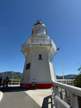 Limanın yanındaki Akaroa Deniz Feneri mavi gökyüzünün altında beyaz ahşap bir yapı gösteriyor. Deniz tarihini ve Akaroa Yeni Zelanda 'nın manzaralı sahil cazibesini simgeliyor.