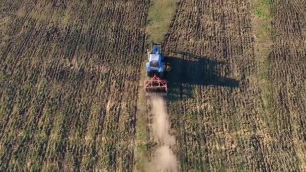 Aufnahmen von Drohnenflügen über Traktor mit Eggenanlage, die Boden auf bewirtschaftetem Acker pflügen, Staubsäule dahinter, Bodenvorbereitung für die Anpflanzung neuer Pflanzen, landwirtschaftliches Konzept, Draufsicht — Stockvideo