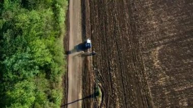 Tarla ve orman arasında tarla boyunca tarla süren bir traktör. Yukarıdan İHA atışı, yaz güneşli hava