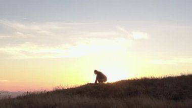Kız dans ediyor, elleri dağlarda gün batımının arka planında düzgün hareketler yapıyor. Şortlu ve kazaklı kız, turizm, seyahat, doğada yoga konsepti.