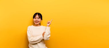 Asyalı güzel kız sarı arka planda beyaz günlük bir elbise giyiyor. Zaferi mutlu bir gülümsemeyle ve kazananın ifadesini kaldırarak kutlayın. Mutlu ifade