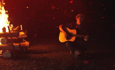 Müzisyenler gece kamp ateşinde gitar çalarlar, müzik çalarak ve eğlenerek dinlenirler..