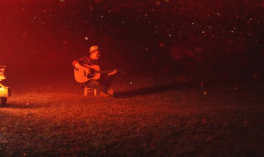 Müzisyenler gece kamp ateşinde gitar çalarlar, müzik çalarak ve eğlenerek dinlenirler..