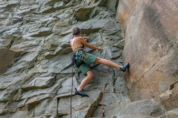 Woman climber with climbing gear equipment climbs on rock wall.