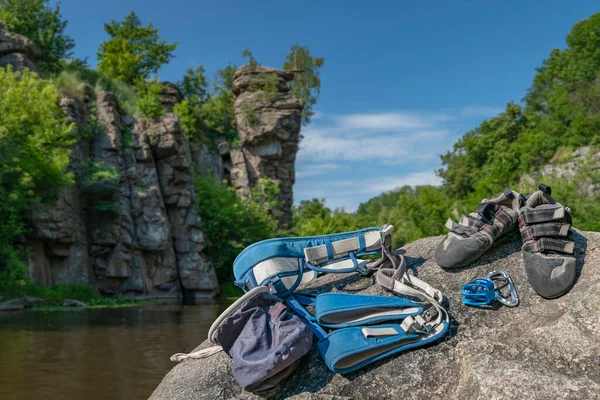 Climbing gear equipment on rock on blurred river canyon background. Climb shoes, belaying carabiners, loops, ropes, bag for magnesia, belay system.