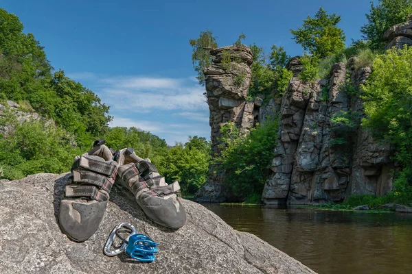 Climbing gear equipment on rock on river canyon background. Climb shoes, belaying carabiners, belay system.