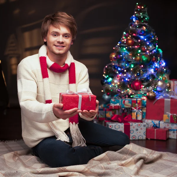 Joven hombre sonriente sosteniendo regalo de Navidad rojo —  Fotos de Stock