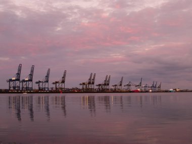 Vinçler İngiltere 'deki Felixstowe rıhtımlarında pembe bir günbatımı gökyüzünün altında gemiler için boş duruyor..