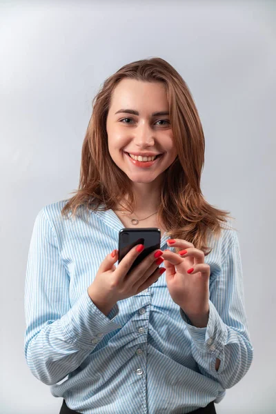 Hermosa chica en una camisa azul con un teléfono sobre un fondo blanco —  Fotos de Stock