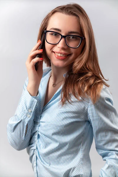 Mavi gömlekli, gözlüklü, beyaz arka planda telefonla konuşan güzel bir kız. — Stok fotoğraf