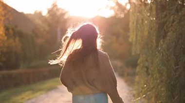 Günbatımında sonbahar parkında koşan ve geriye bakan neşeli kadın. Sıcak altın ışık, kaygısız ruh hali, mutluluk ve dışarıda özgürlük..
