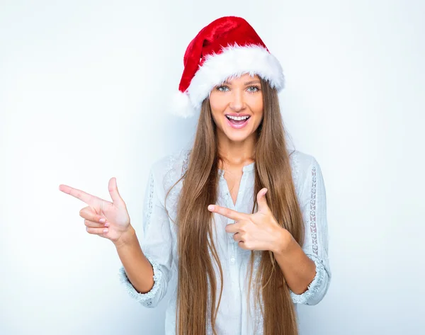 Girl in santa hat pointing at something — Stockfoto