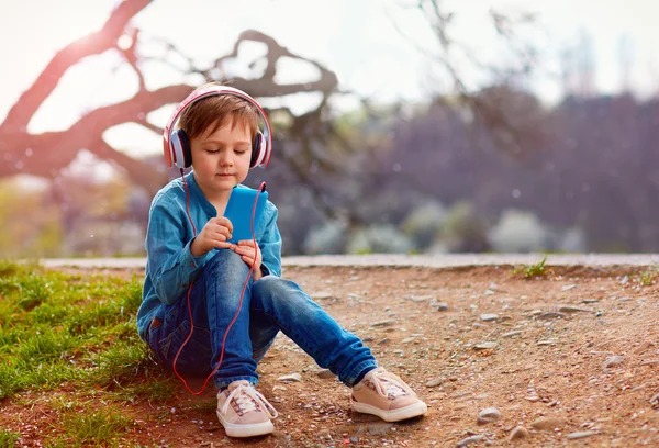 Милий хлопчик з навушниками слухає музику в парку — стокове фото