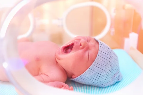 Newborn baby yawning while lying in infant incubator — Stock Photo, Image