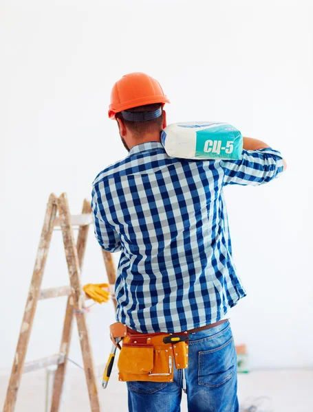 Hombre en casco lleva una bolsa de cemento para fines de construcción — Foto de Stock