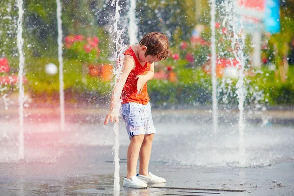 Excited boy having fun between water jets, in fountain. Summer in the city — Stock Photo, Image