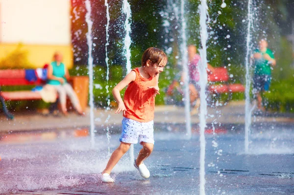 Aufgeregter Junge, der sich zwischen Wasserstrahlen im Springbrunnen vergnügt. Sommer in der Stadt — Stockfoto