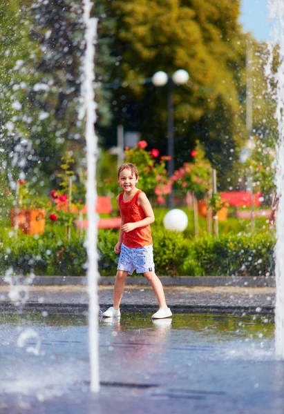 Ophidset dreng have det sjovt mellem vandstråler, i springvand. Sommer i byen - Stock-foto