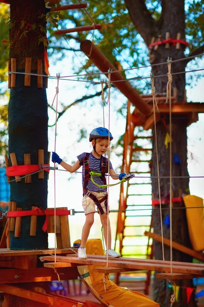 Chico joven pasando la ruta de cable alto entre los árboles, deporte extremo en el parque de aventuras — Foto de Stock