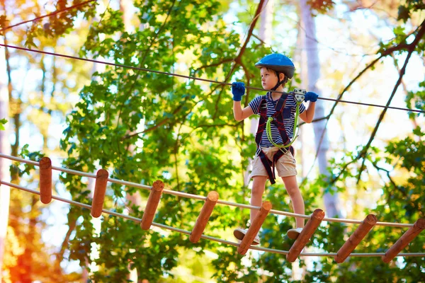 Chico joven pasando la ruta de cable alto entre los árboles, deporte extremo en el parque de aventuras — Foto de Stock