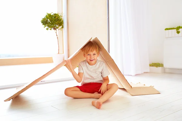 Menino feliz bonito jogando com caixa de papelão como com casa de brinquedo — Fotografia de Stock