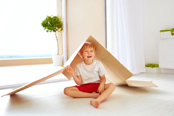 Lindo niño feliz jugando con caja de cartón como con casa de juguete —  Fotos de Stock